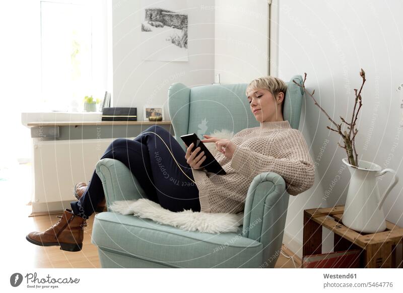 Entspannte Frau sitzt in einem Sessel zu Hause und benutzt ein Tablet Deutschland WLan Wireless Lan W-Lan Wifi bequem ausruhen Rast Erholung erholen Wohnung