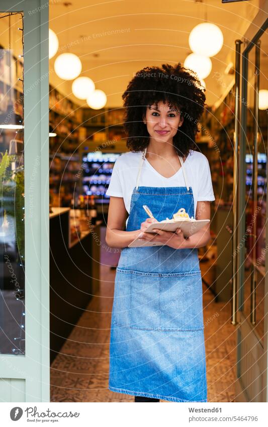 Porträt einer lächelnden Frau mit Klemmbrett, die in der Eingangstür eines Geschäfts steht Klemmbretter Shop Laden Läden Geschäfte Shops Portrait Porträts