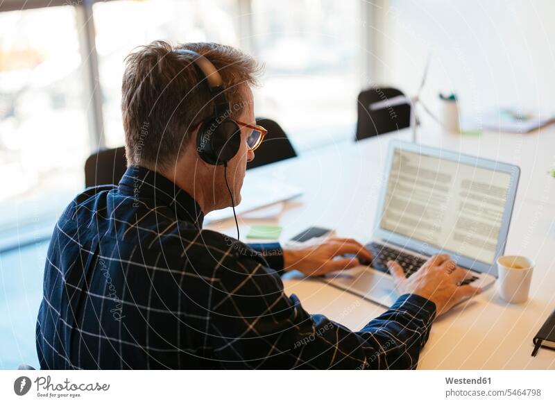Geschäftsmann trägt Kopfhörer mit Laptop am Schreibtisch im Büro Notebook Laptops Notebooks Businessmann Businessmänner Geschäftsmänner Arbeitstisch
