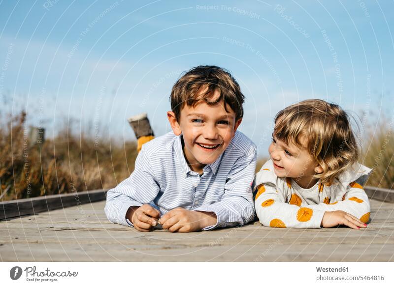 Porträt eines Jungen und seiner kleinen Schwester, die Seite an Seite auf der Promenade liegen und Spaß haben Harmonie harmonisch nebeneinander Schwestern