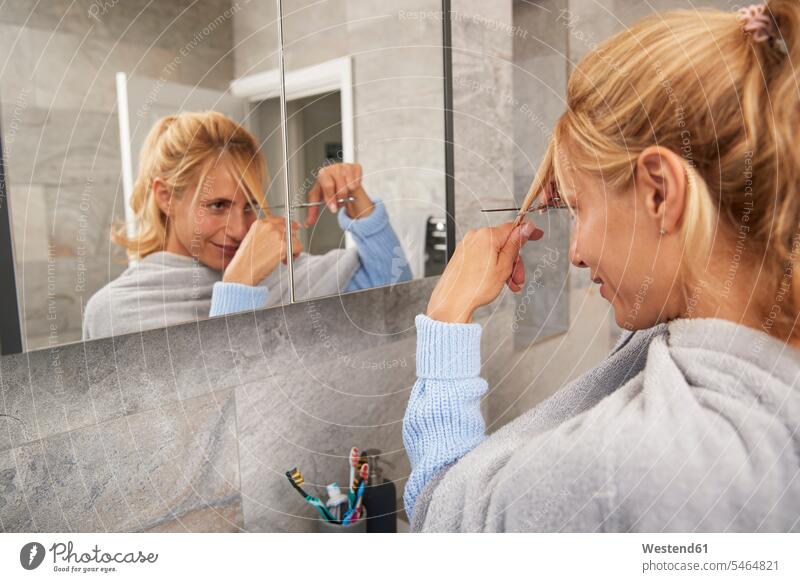 Reife Frau schaut in den Spiegel und schneidet sich zu Hause die Haare selbst Farbaufnahme Farbe Farbfoto Farbphoto Innenaufnahme Innenaufnahmen innen drinnen