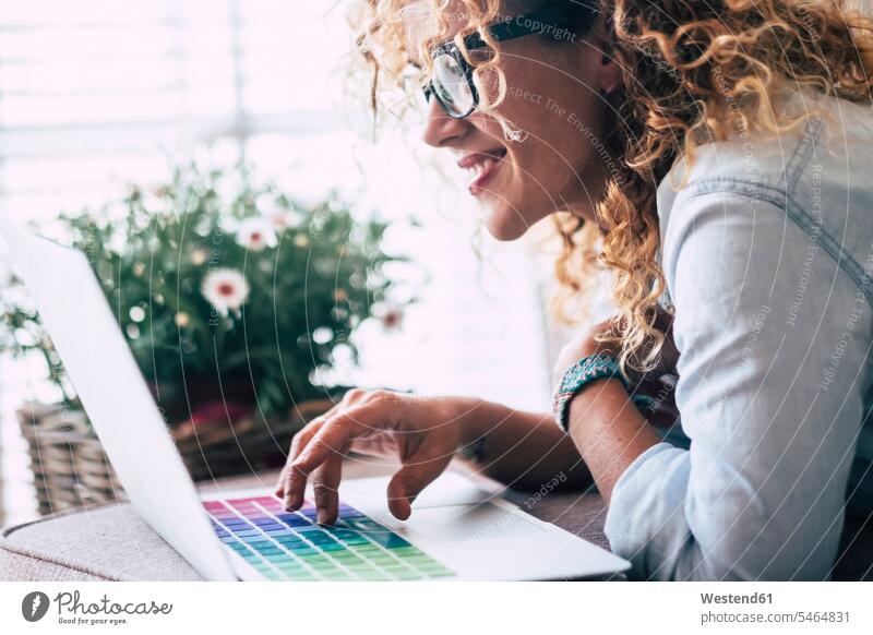 Lächelnde Frau liegt auf der Couch zu Hause mit Laptop Fenster Technologie Technologien Technik blond blonde Haare blondes Haar Mobilität mobil Locken