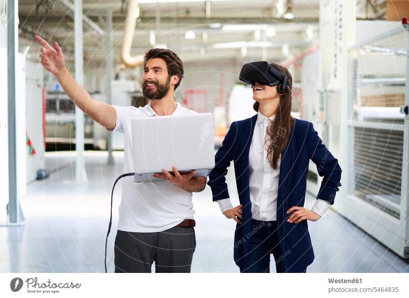 Mann mit Laptop und Geschäftsfrau mit VR-Brille in Fabrik Arbeitskollege Arbeitskollegen Kollege Job Berufe Berufstätigkeit Beschäftigung Jobs geschäftlich