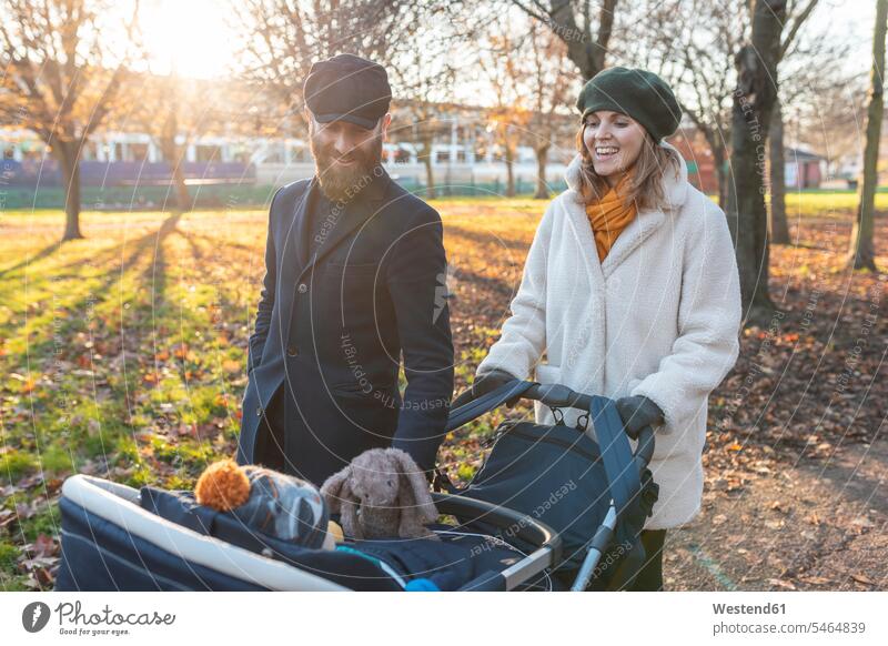 Glückliches Paar mit kleinem Sohn in einem Kinderwagen im Park Jacken Mützen freuen Frohsinn Fröhlichkeit Heiterkeit geniessen Genuss glücklich sein