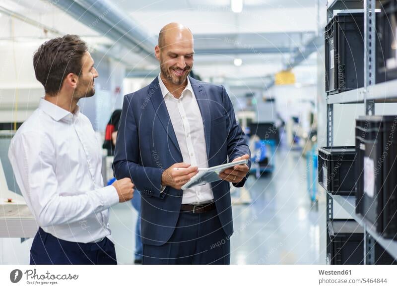 Lächelnder Geschäftsmann benutzt digitales Tablett, während er einem Ingenieur bei einer Diskussion in der Industrie zuhört Farbaufnahme Farbe Farbfoto