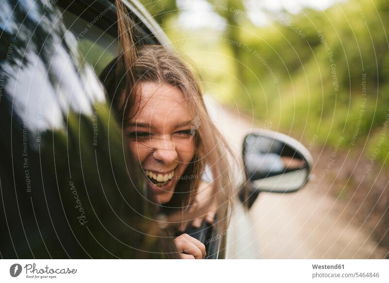 Unbeschwerte junge Frau lehnt sich aus dem Autofenster KFZ Verkehrsmittel Automobil Autos PKW PKWs Wagen fahrend fahrende fahrender fahrendes verreisen
