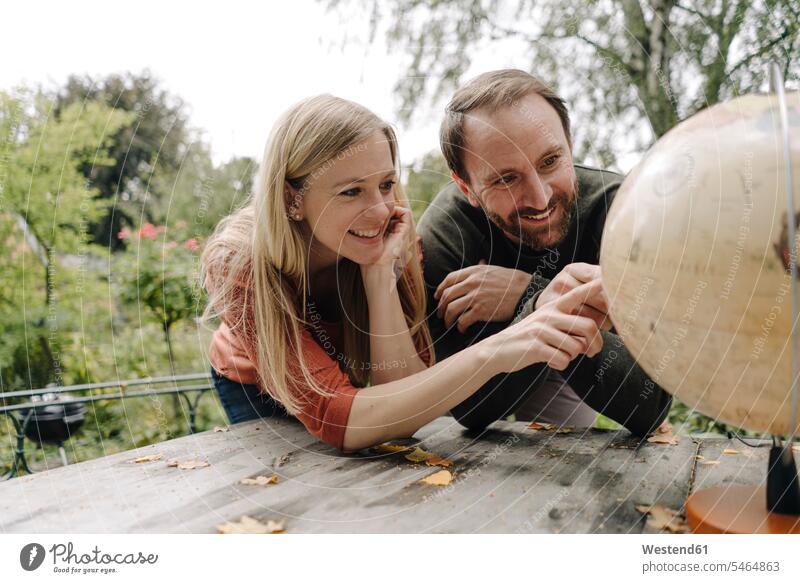Glückliches Paar, das eine Reise plant und den Globus im Freien betrachtet Erdkugel Globen Weltkugel Tische Holztische entdecken Jahreszeiten freuen
