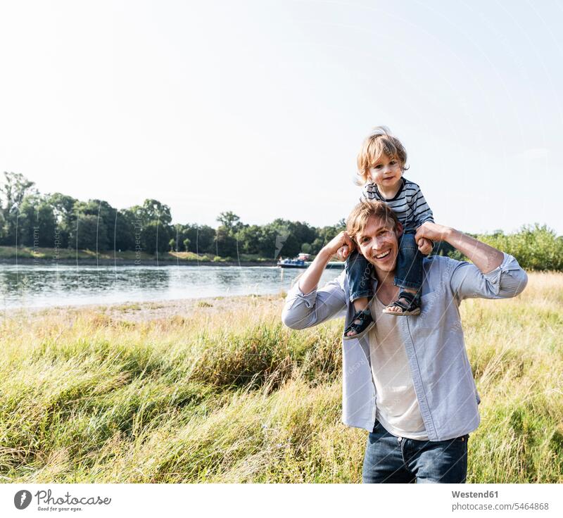 Vater und Sohn haben Spaß am Fluss an einem schönen Sommertag Deutschland auf den Schultern auf der Schulter Kindheit Spaziergang Flussufer Gemeinsamkeit