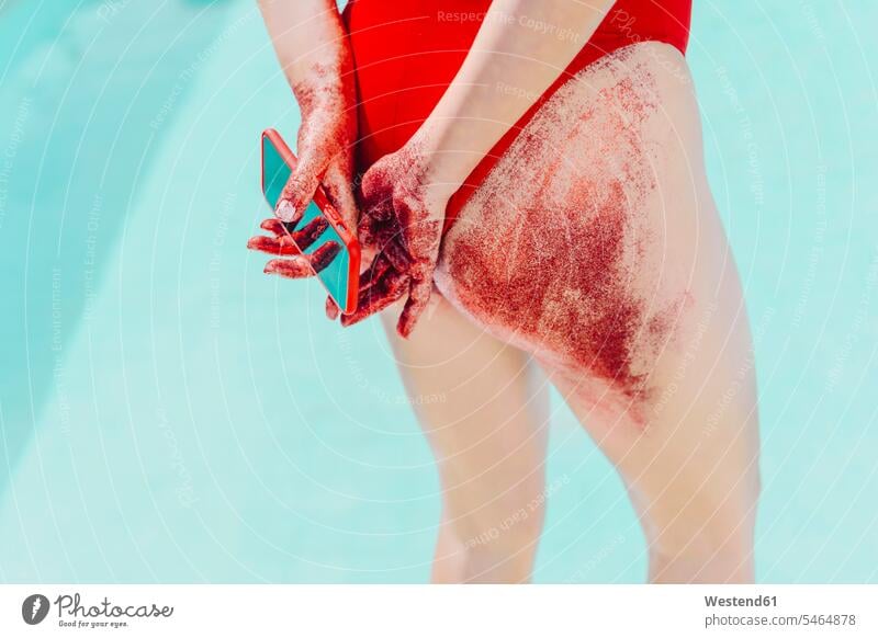 Rückansicht einer Frau, die ein Mobiltelefon hält, dessen Boden mit rotem Sand bedeckt ist Badebekleidung Badeanzuege Badeanzüge Telekommunikation telefonieren