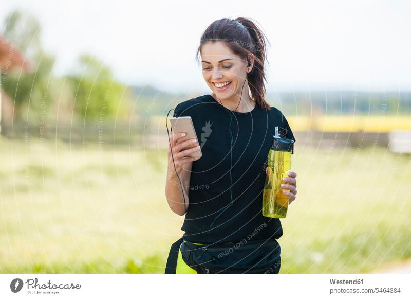 Sportliche Frau mit Smartphone in Kühlpause Ohrhörer Wasserflasche Flasche Flaschen Wasserflaschen Trinkpause Trinkpausen iPhone Smartphones Musik hören