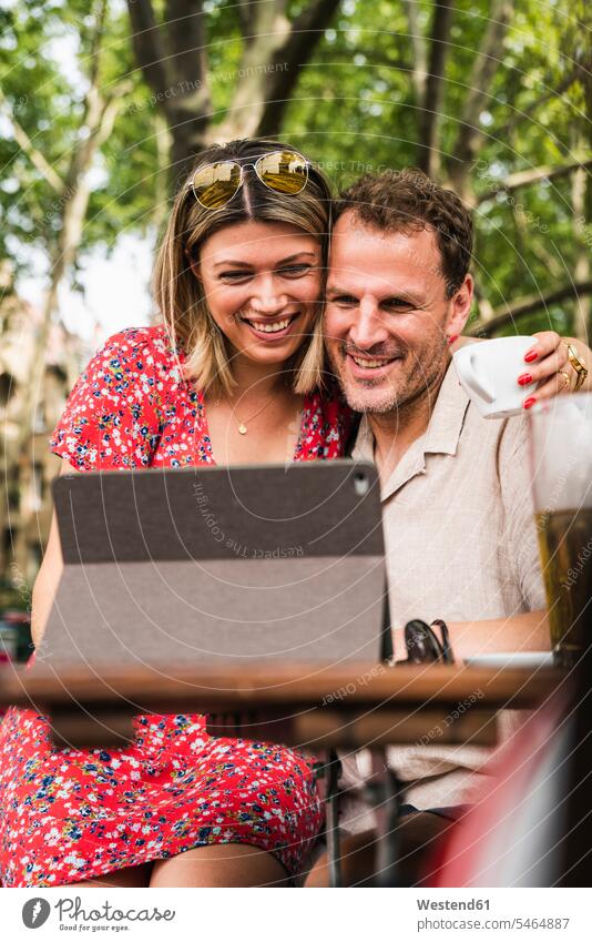 Lächelndes Paar, das sich in einem Café im Freien Tabletten teilt Teilen Sharing Cafe Kaffeehaus Bistro Cafes Cafés Kaffeehäuser Tablet Computer Tablet-PC