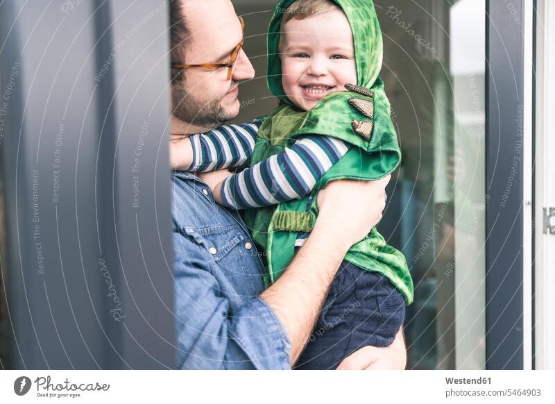 Vater trägt glücklichen Sohn in einem Kostüm an der Terrassentür zu Hause tragen transportieren Terrassentuer Zuhause daheim Maskenkostüm Maskenkostüme