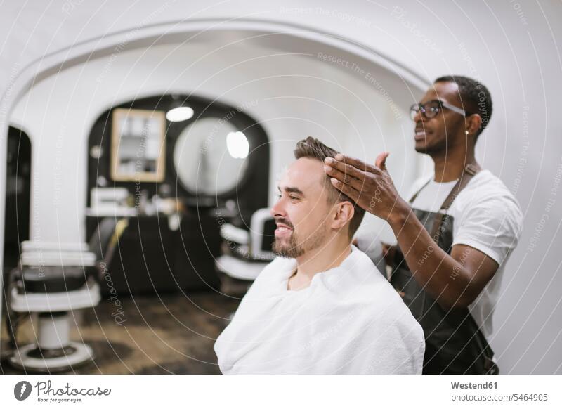 Lächelnder Friseur beendet Haarschnitt eines Kunden im Friseurladen Leute Menschen People Person Personen Kundschaft Job Berufe Berufstätigkeit Beschäftigung