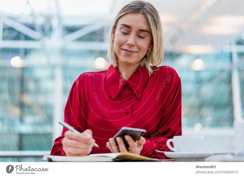 Junge Geschäftsfrau mit Handy macht Notizen in einem Cafe Job Berufe Berufstätigkeit Beschäftigung Jobs geschäftlich Geschäftsleben Geschäftswelt