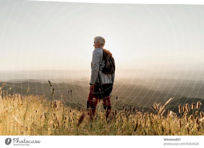 Aktiver älterer männlicher Wanderer, der bei Sonnenuntergang auf einem Berg steht und die Landschaft betrachtet Farbaufnahme Farbe Farbfoto Farbphoto Spanien