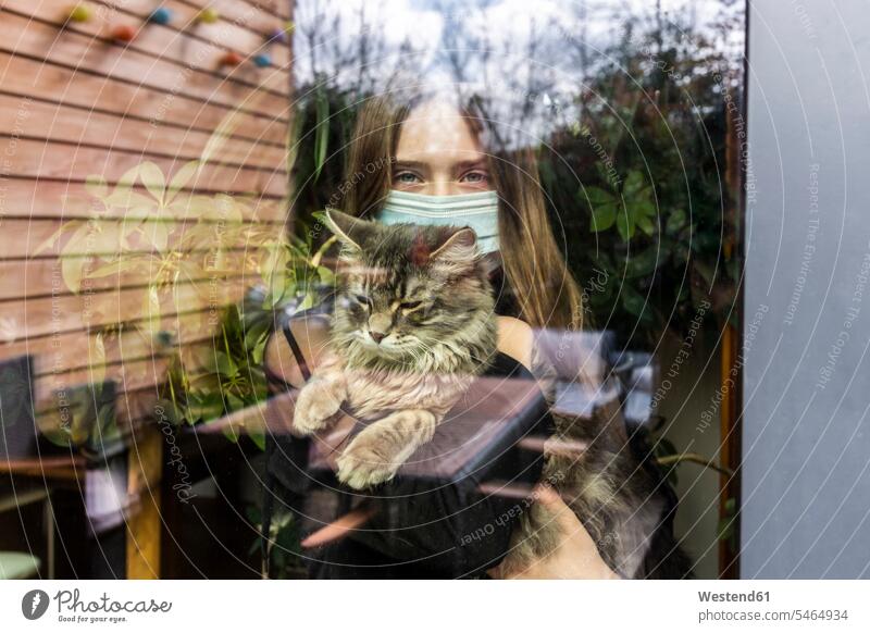 Porträt eines Mädchens mit chirurgischer Maske und Katze hinter Fensterscheibe Tiere Tierwelt Haustiere Katzen Fensterscheiben pessimistisch schwarzseherisch