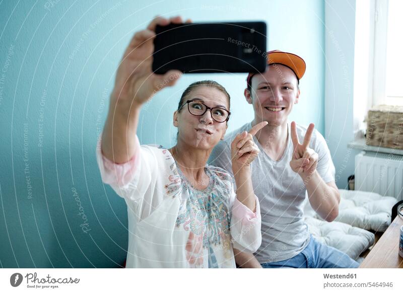 Mutter und Sohn sitzen am Küchentisch und machen Selfies mit ihrem Smartphone Deutschland Besuch Basecap Schirmmuetze Mütze Schirmmütze Muetze Kopfbedeckung