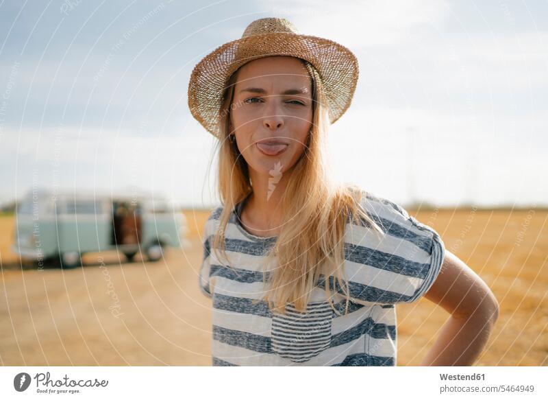 Porträt einer jungen Frau am Wohnmobil in ländlicher Landschaft, die ihre Zunge herausstreckt weiblich Frauen Landschaften Campingbus Portrait Porträts