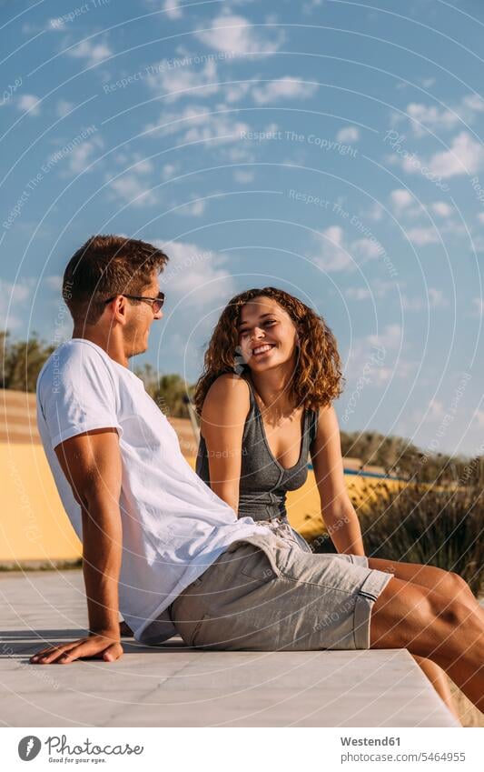 Glückliches junges Paar sitzt auf einem Pier Touristen Brillen Sonnenbrillen Flirt sitzend reden Jahreszeiten sommerlich Sommerzeit entspannen relaxen