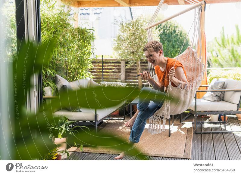 Fröhliche Frau, die über Handy telefoniert, während sie sich auf der Veranda schaukelte, von innen gesehen Farbaufnahme Farbe Farbfoto Farbphoto Deutschland