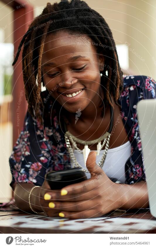 Porträt einer glücklichen jungen Frau, die ihr Telefon überprüft Leute Menschen People Person Personen Afrikanisch Afrikanische Abstammung dunkelhäutig Farbige