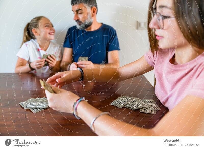 Vater mit zwei Töchtern spielt zu Hause Karten auf einem Holztisch Spielkarten T-Shirts Tische Holztische Spiele Gesellschaftsspiele Glücksspiele Kartenspiele