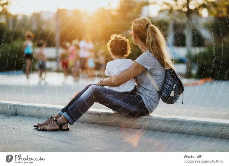Mther sitzt mit ihrem kleinen Sohn bei Sonnenuntergang auf einem Platz Plätze Plaetze Sonnenuntergänge Mutter Mami Mutti Mütter Mama sitzen sitzend Söhne