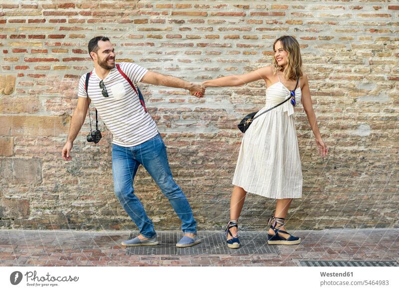 Glückliches Paar, das sich an den Händen hält und in entgegengesetzte Richtungen an einer Backsteinmauer läuft Pärchen Paare Partnerschaft glücklich