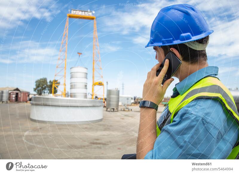 Mann in Arbeitskleidung auf der Baustelle telefoniert Arbeitsbekleidung Männer männlich Handy Mobiltelefon Handies Handys Mobiltelefone Baustellen telefonieren