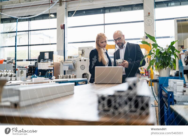 Geschäftsmann und Geschäftsfrau mit Laptop, die ein Werkstück in einer Fabrik untersuchen Notebook Laptops Notebooks prüfen Fabriken Businessmann Businessmänner