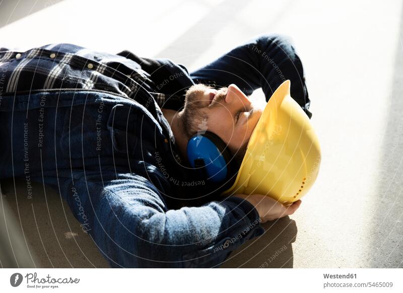 Nahaufnahme eines Bauarbeiters mit Händen hinter dem Kopf auf dem Boden schlafend in einem renovierenden Haus Farbaufnahme Farbe Farbfoto Farbphoto Deutschland