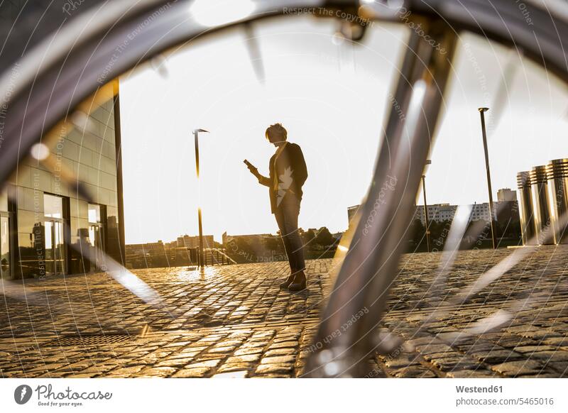 Frau benutzt Mobiltelefon hinter Fahrradreifen bei Sonnenuntergang Bikes Fahrräder Räder Rad weiblich Frauen Sonnenuntergänge Handy Handies Handys Mobiltelefone
