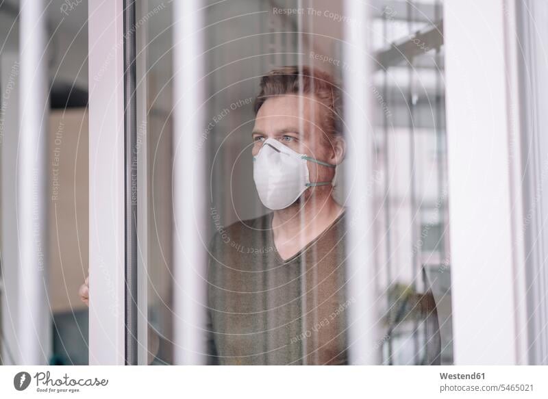 Bildnis eines Mannes mit Schutzmaske hinten am Fenster Fensterscheiben Glasscheiben Gesund geschützt schützen Absicherung gefaehrlich Gefahren gefährlich am Tag