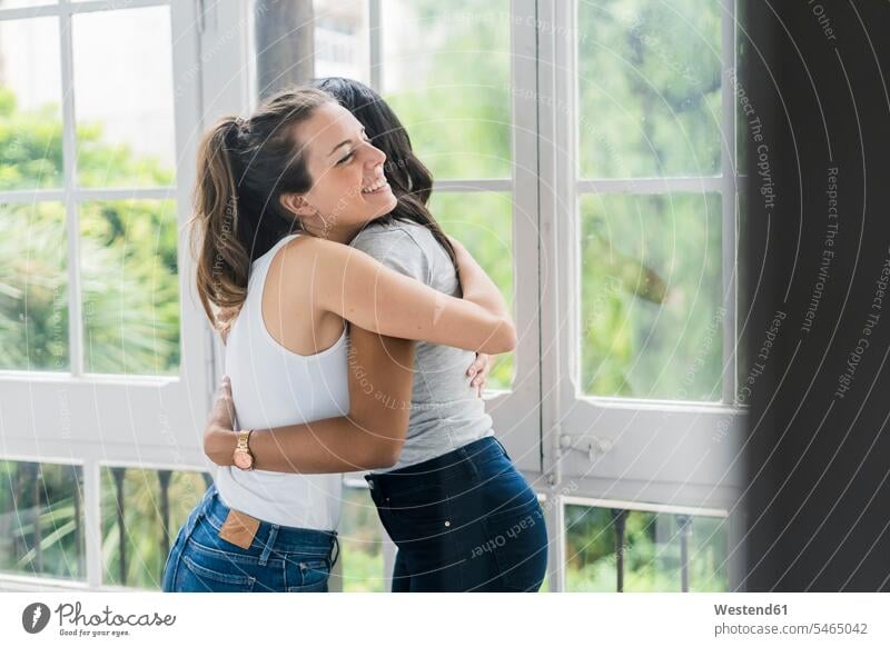 Zwei glückliche Freundinnen umarmen sich am Fenster Umarmung Umarmungen Arm umlegen Frau weiblich Frauen Glück glücklich sein glücklichsein Freunde Freundschaft