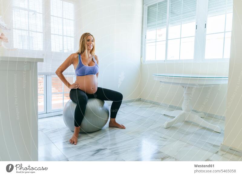 Lächelnde schwangere Frau sitzt auf Fitness-Ball Fitnessball Gymnastikball Sitzball sitzen sitzend Schwangere weiblich Frauen lächeln Erwachsener erwachsen