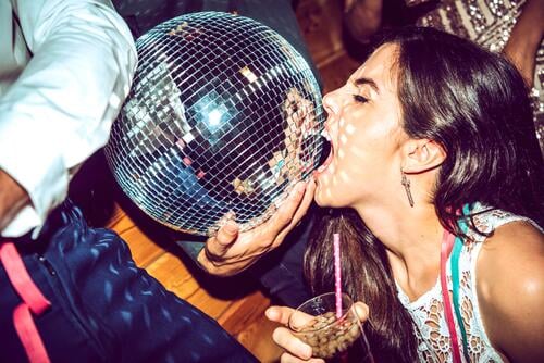 Junge Frau mit geschlossenen Augen hält Getränk und beißende Discokugel in glamouröser Party Farbaufnahme Farbe Farbfoto Farbphoto Innenaufnahme Innenaufnahmen