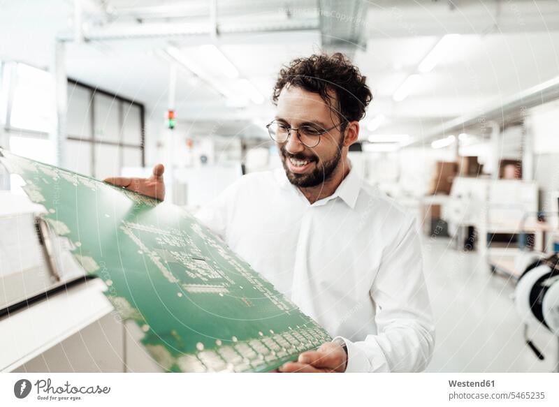 Lächelnder männlicher Techniker analysiert großen Computerchip in der Industrie Farbaufnahme Farbe Farbfoto Farbphoto Deutschland Innenaufnahme Innenaufnahmen