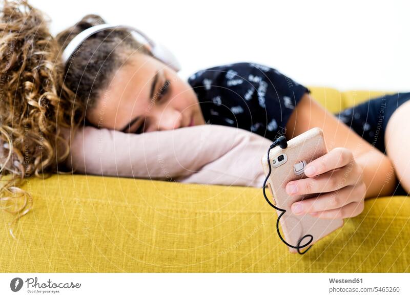 Mädchen auf der Couch liegend zu Hause hören Musik mit Kopfhörer und Smartphone Sofa Couches Liege Sofas iPhone Smartphones weiblich Zuhause daheim liegt hoeren