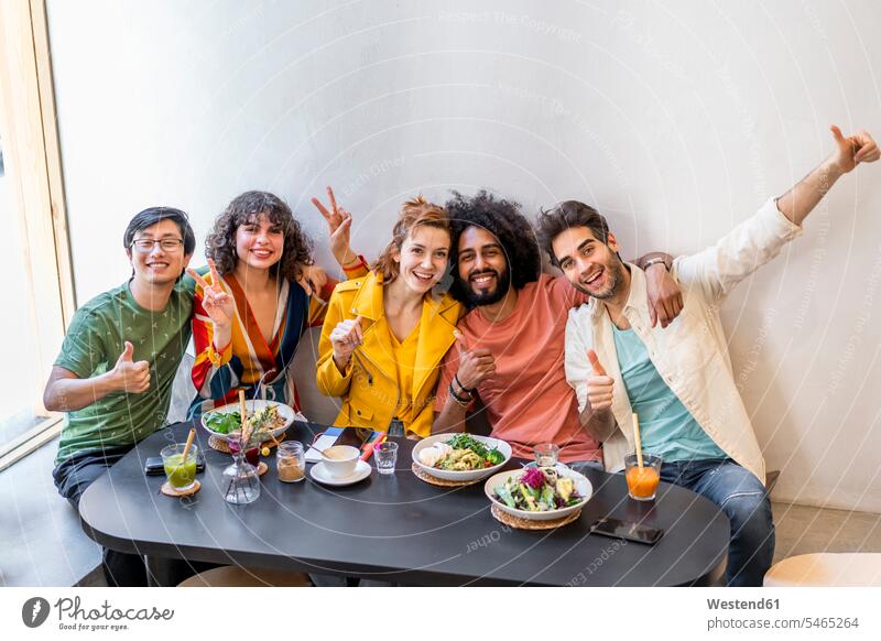 Porträt einer glücklichen Gruppe von Freunden in einem Restaurant Gläser Trinkglas Trinkgläser Tische sitzend sitzt Arm umlegen Umarmung Umarmungen begeistert