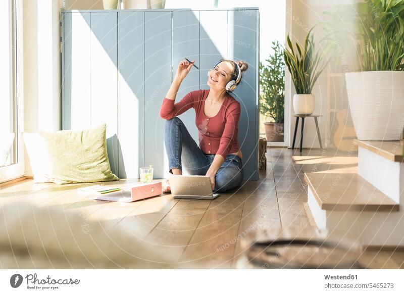 Frau mit Kopfhörer sitzt am Fenster zu Hause mit Laptop weiblich Frauen Zuhause daheim sitzen sitzend Kopfhoerer Notebook Laptops Notebooks Erwachsener