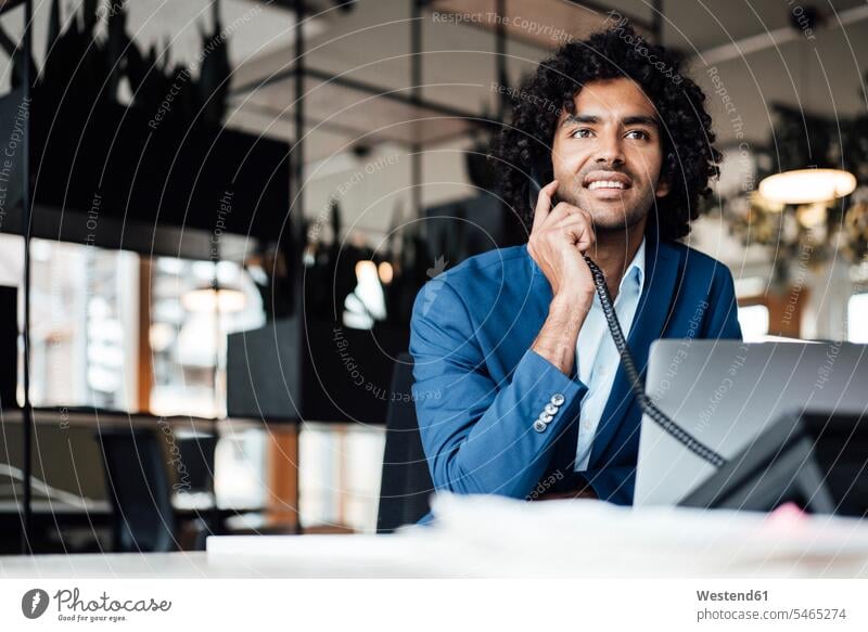 Lächelnde Geschäftsmann am Telefon sprechen, während mit Laptop im Büro sitzen Farbaufnahme Farbe Farbfoto Farbphoto Deutschland Innenaufnahme Innenaufnahmen