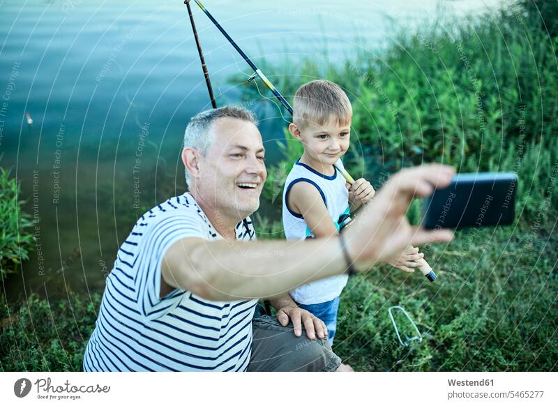 Großvater und Enkel machen Selfie mit Smartphone am Seeufer iPhone Smartphones Opa Großpapa Großpapas Opas Opi Großväter Opis Selfies Enkelsöhne Enkelsohn Handy