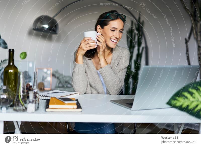 Glückliche junge Frau zu Hause mit Laptop auf dem Schreibtisch weiblich Frauen Notebook Laptops Notebooks Arbeitstisch Schreibtische glücklich glücklich sein