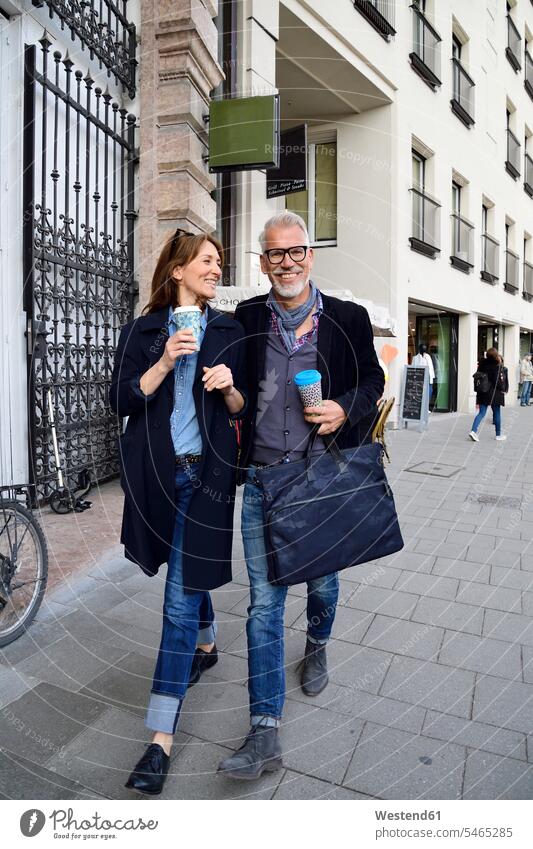 Lächelndes reifes Paar mit wiederverwendbaren Bambusbechern beim Spaziergang in der Stadt München Muenchen Wiederverwendung Touristin Coffee to go zum mitnehmen