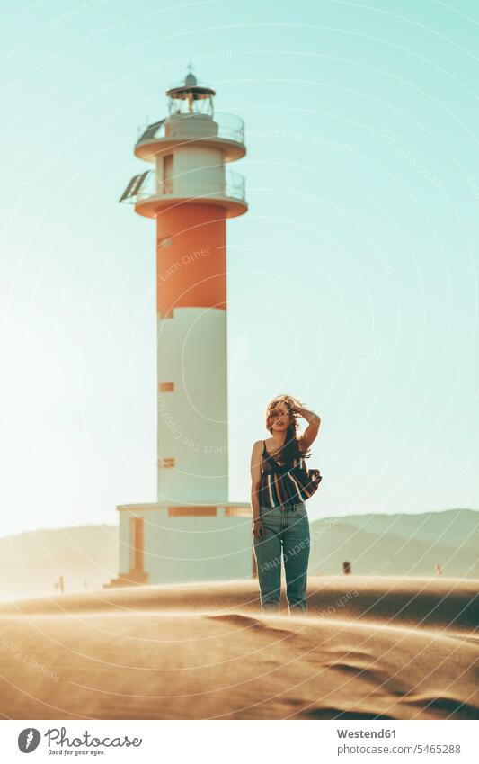 Junge Frau mit windgepeitschtem Haar steht in Wüstenlandschaft am Leuchtturm Landschaft Landschaften weiblich Frauen Leuchttürme wehen wehend stehen stehend
