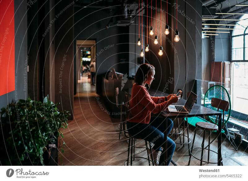 Junge Frau benutzt Laptop und Smartphone in einem Café Job Berufe Berufstätigkeit Beschäftigung Jobs geschäftlich Geschäftsleben Geschäftswelt Geschäftsperson