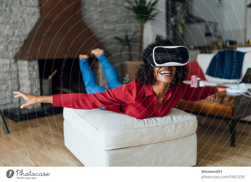 Frau liegt auf Sitzmöbeln, trägt VR-Brille und tut so, als würde sie fliegen Flugzeug spielen so tun als ob man fliegt Fliegen spielen Flieger spielen