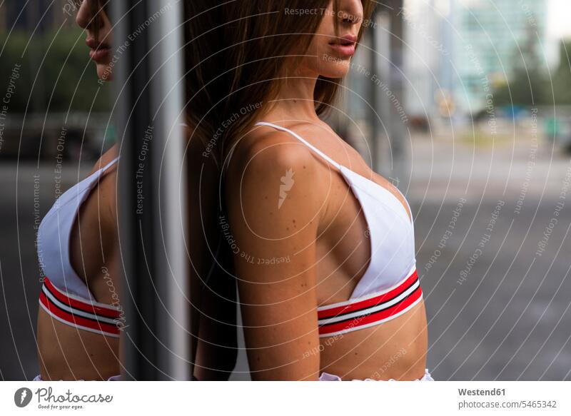 Nahaufnahme einer attraktiven jungen Frau in Sportkleidung, die sich an eine Glasfront eines Gebäudes lehnt Sportbekleidung Sportdress Kleidung Glasfassade