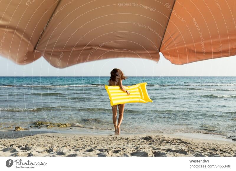 Junge Frau mit gelber Luftmatratze am Strand Luftmatratzen gehend geht sommerlich Sommerzeit geniessen Genuss gelbes erfrischen erfrischend frei Muße