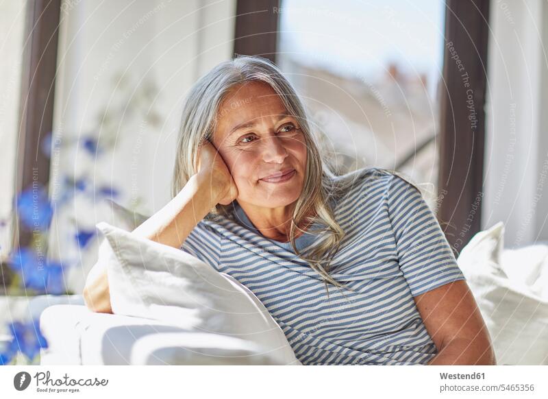 Lächelnde Frau entspannt auf dem Sofa im Wohnzimmer Deutschland Innenaufnahme Innenaufnahmen innen drinnen Tag Tageslichtaufnahme Tageslichtaufnahmen
